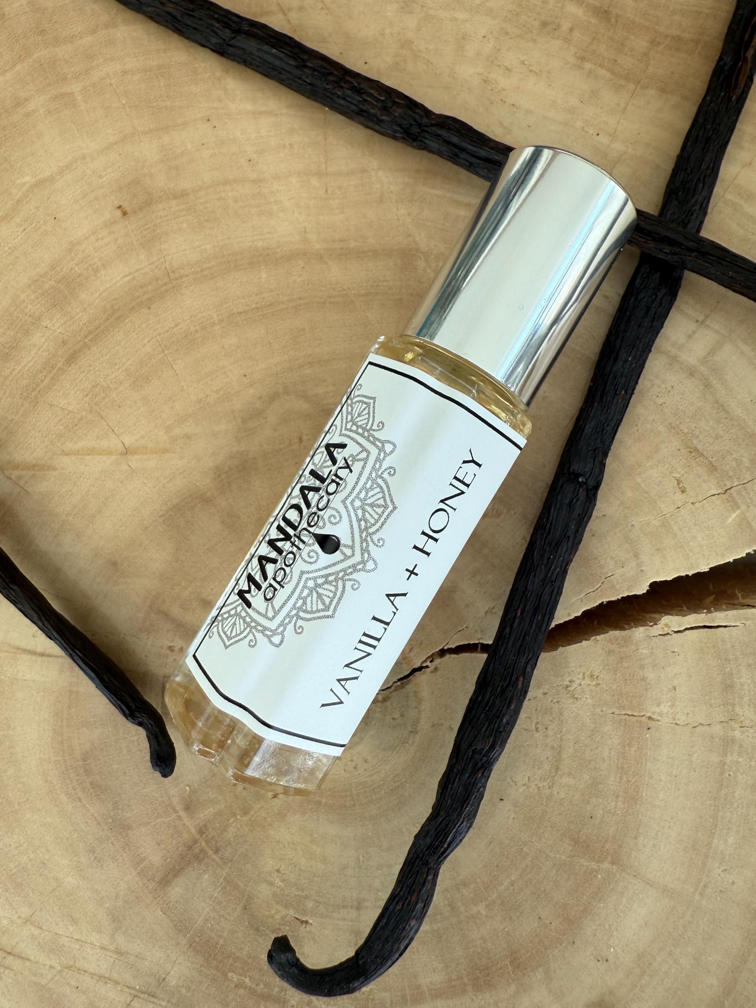 roll-on natural perfume of vanilla and honey displayed on a block of wood and surrounded by whole vanilla beans.